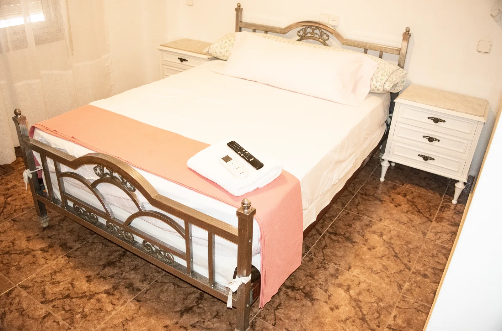 Habitación con cama de forja y mesita blanca